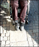 Framdelen av en rullstol med ngon sittandes i, p kullerstenar.