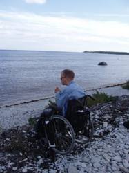 Håkan Pettersson sitter i en rullstol på en stenig strand och ser ut över havet.